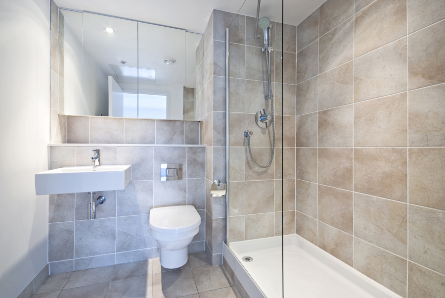 Modern en suite bathroom with large shower, toilet and wash basin in beige natural with natural stone tiled walls.